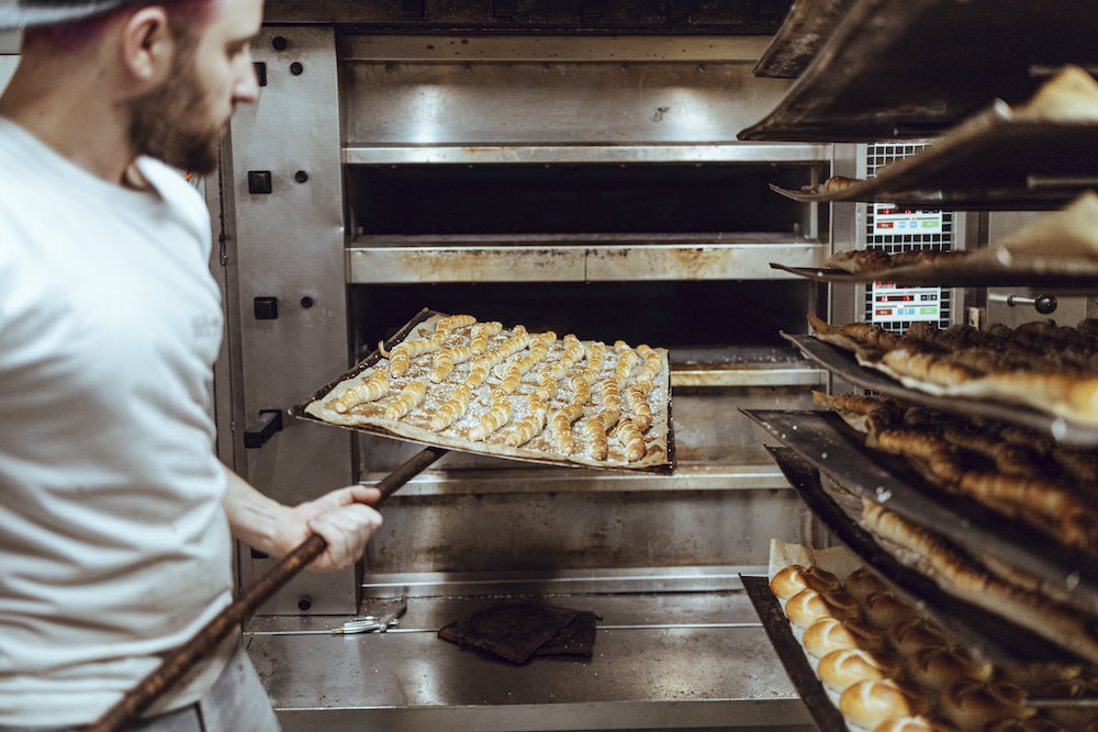 Ein Mitarbeiter in der Backstube holt frische Dampflstangerl für Geschäftskunden aus dem Backofen